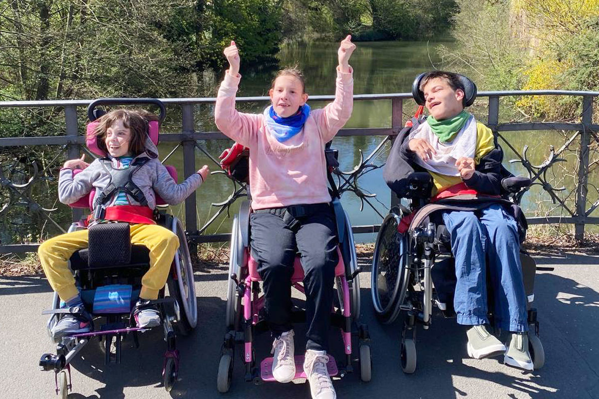 Drei Jugendluche sitzen im Rollstuhl und machen ein Foto auf einer Brücke. 
